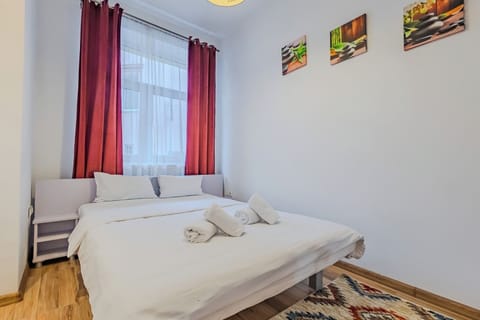 Queen-size bed with white hotel-quality linens and rolled towels. Red curtains, ethnic-print rug and landscape artwork. Blackout curtains for restful sleep. Maia Studio in Old Town, Brasov, sleeps 3.