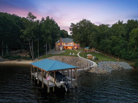 Twilight settles over the waterfront retreat, with a covered dock, softly lit shoreline, and peaceful wooded setting.