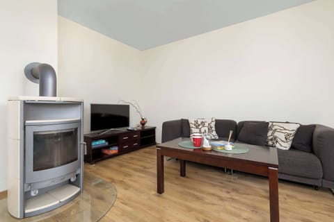 A modern fireplace stands in the corner of a living area adjacent to a dark TV console. Two plush dark grey sofas and a low wooden coffee table form a comfortable lounge arrangement.