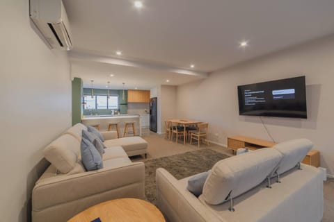 Modern central Christchurch lounge with two sofas, area rug, heat pump, wall-mounted TV, dining space and breakfast bar.