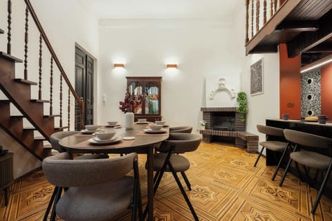 Looking across the dining table, the view reveals a decorative corner fireplace, ornate wooden stairs, and terracotta kitchen accents.