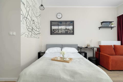 The sleeping area includes a bed with a white tray beneath a city map wall graphic. A small orange sofa sits in the corner by the window.