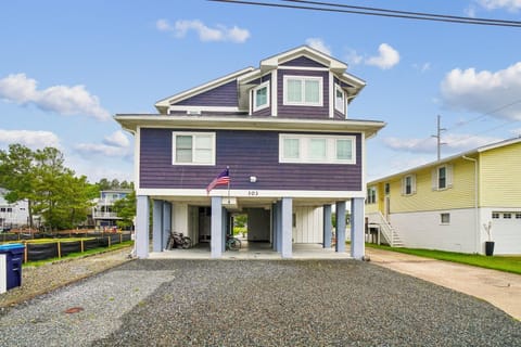A distinctive coastal property elevated on sturdy stilts, displaying address number 103 and welcoming arrivals with covered parking beneath the main living quarters.