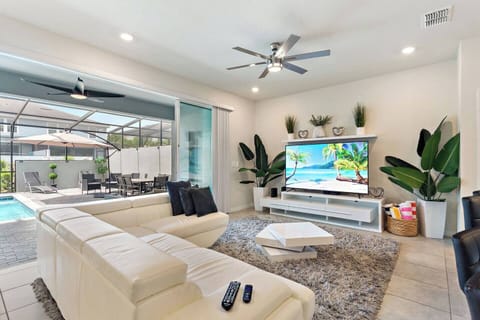 Bright open-concept living room with a 75" Smart TV, cable, and 1 GIG high-speed Wi-Fi. Spacious 5-person sofa (pullout), ceiling fan, and patio doors leading directly to the private pool—perfect for families to relax and unwind together.