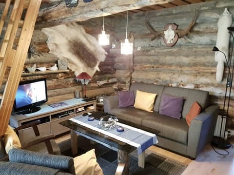 Cozy living room with a comfortable sofa, TV and coffee table under warm log walls.
