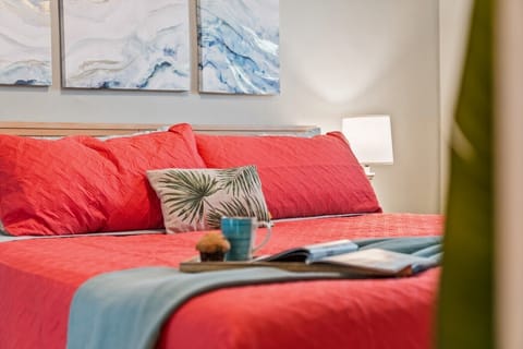 Primary Suite King Bed Detail: Unwind in total luxury on this plush king bed, complete with vibrant coral bedding, layered accent pillows, soft bedside lamp lighting, and a breakfast-in-bed tray set up for a relaxing vacation morning.