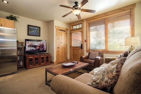 Unwind in your cozy living space with plush seating, entertainment ready, and warm natural light streaming through charming wood-framed windows inviting relaxation after your mountain adventures.
