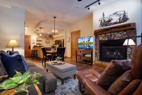 Relax in your inviting open-concept living space featuring a stone fireplace, plush seating, and mountain-inspired decor. Your fully equipped kitchen and cozy dining area await memorable evenings together.