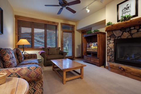 Unwind in your cozy living room with a crackling stone fireplace, plush patterned seating, and mountain charm—perfect for evenings after exploring the slopes.