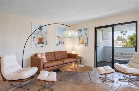 Your living room awaits with mid-century flair—tan leather sofa, stylish seating, and desert-inspired artwork. Step out to your private patio and soak up the California sunshine.