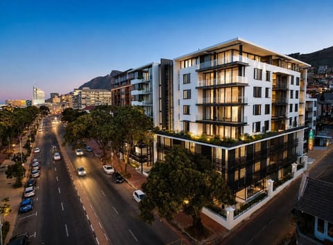 Exterior: Striking multi-story residence with glass-fronted balconies, landscaped terraces, and contemporary architecture, positioned along a tree-lined city street with mountain scenery beyond.