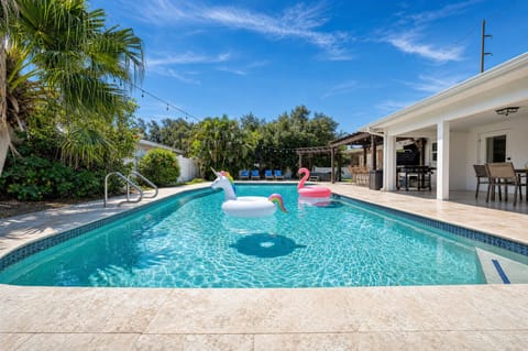 Wooden loungers lead straight to the pool where flamingo and unicorn floats bob lazily, palm trees framing a true tropical retreat.