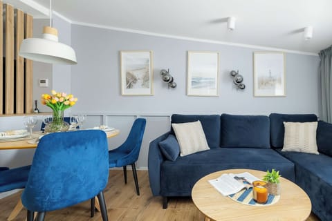 A bright and cozy living room with a blue sofa, armchairs, and a small round coffee table. Large windows and light colors create a pleasant and inviting atmosphere.