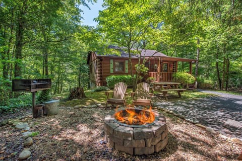 A cozy log cabin nestled in lush woodland, featuring an outdoor fire pit, Adirondack chairs, BBQ facilities, and covered porch—your private forest retreat awaits.