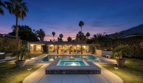 A stunning resort-style property featuring a sparkling pool and spa set among lush gardens with mountain views, ideal for evening relaxation under swaying palms.