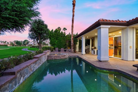 Poolside patio and covered home exterior beneath a colorful sunset sky.