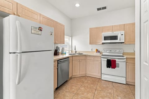 Kitchen with light wood cabinets, white appliances, stainless steel dishwasher, and beige tile flooring.