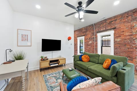 Relax in the open living room with charming exposed brick, a plush green sofa, and Roku TV. You are just minutes from riverfront strolls at Promenade Park and local dining on The Landing.