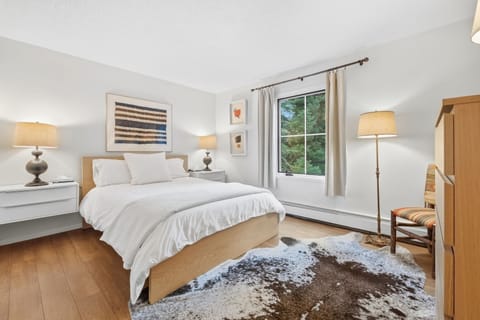 A well-lit bedroom with a wooden bed, patterned cowhide rug, and green exterior views.
