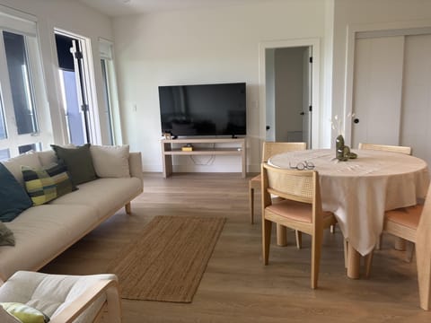 The living and dining area features light wood floors, a beige sofa with colorful cushions, and a round table with woven chairs.