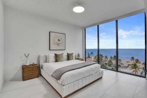 Primary bedroom with king bed and floor-to-ceiling windows framing a direct ocean and palm tree view.
