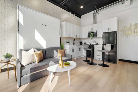 🌿 Studio living framed by leafy views—warm wood floors and floor-to-ceiling windows bring the outside in.