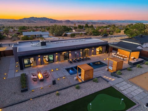 Twilight desert retreat with a pool, fire pit lounge, putting green, outdoor dining, and mountain views.