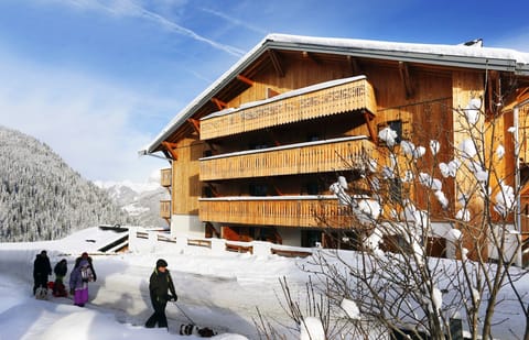 Wooden building with balconies and people walking in snow