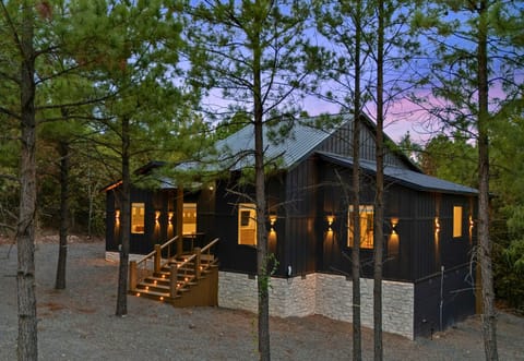 The cabin feels right at home among the trees, with warm exterior lighting and a spacious outdoor setting that makes a welcoming first impression.