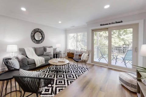 Geometric patterns and woven textures create a modern coastal vibe in this bright living area. Soft morning light pours through sliding glass doors, connecting the smooth wood floors to a private leafy balcony.