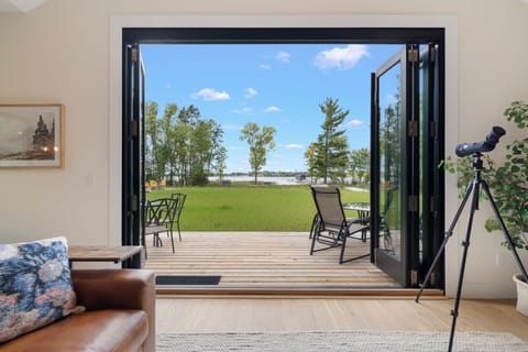 Step through your open glass doors onto a private deck where a peaceful waterfront setting awaits. Settle into comfortable seating surrounded by expansive lawns and trees, with a serene lake view stretching before you.