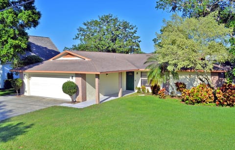 Ranch-style home exterior with large oak tree, attached garage, and tropical landscaping