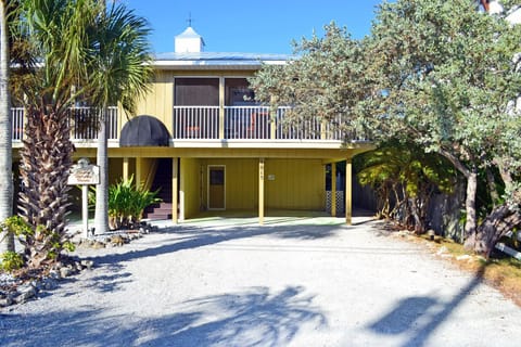 Front of the home with wraparound porch and mature tropical landscaping