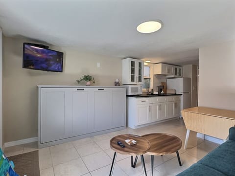 An open living space featuring a TV console, sofa, coffee table, and kitchen in the background.