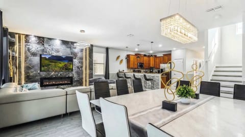 Elegant open-concept living area with a modern fireplace, marble accents, crystal chandelier, and a stylish kitchen.