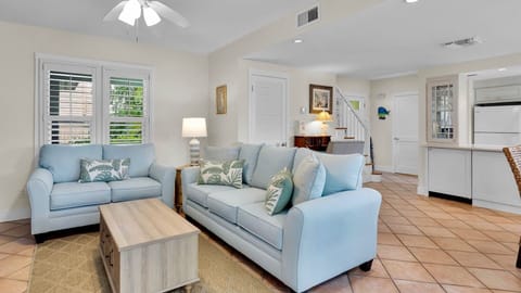Sink into plush blue sofas where coastal charm meets modern comfort. Your peaceful retreat features tile floors and natural light streaming through plantation shutters.