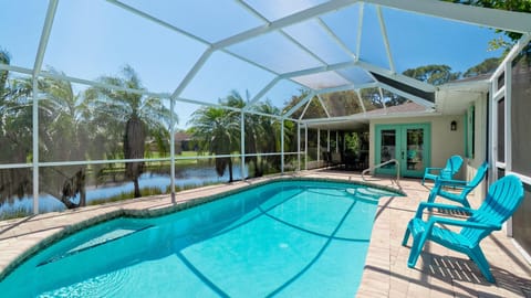Screened pool area with turquoise Adirondack chairs on brick pavers, overlooking palm trees and a lake.