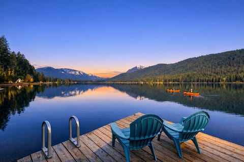 Pristine mountain lake with snow-capped peaks reflects vibrant sunrise colors, while kayakers explore the peaceful waters.