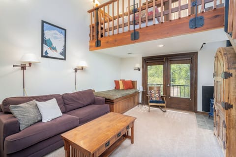 Unwind in your open, light-filled living room with cozy seating, warm wood accents, and a private balcony overlooking lush greenery—perfect for relaxing after a day of adventure.
