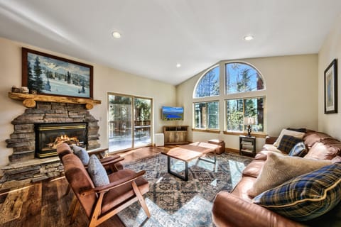 Cozy up by the crackling stone fireplace while enjoying mountain views through stunning arched windows in this warm, inviting living space.