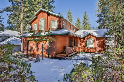 Charming mountain cabin with snow-dusted grounds surrounded by towering pine trees in a peaceful forest setting.