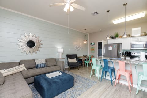 Relax in your bright open-concept living space featuring colorful coastal charm, a fully equipped kitchen, and comfortable seating for memorable vacation moments.