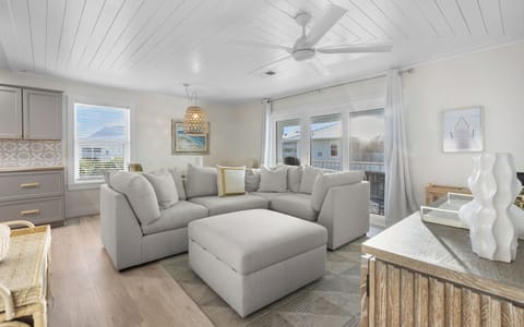 Sink into plush gray sectionals beneath your elegant ceiling fan, where coastal charm meets modern comfort in this bright, airy living space.