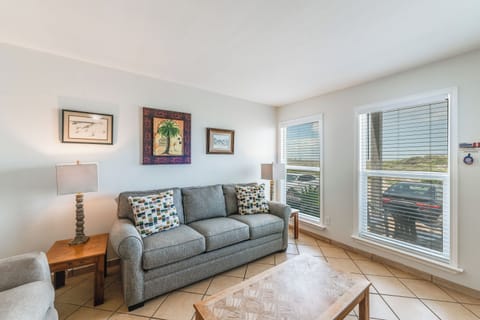 Relax in your bright corner living room with comfy seating, coastal artwork, and large windows flooding the space with natural light.
