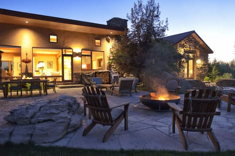 Gather around your private fire pit as twilight settles over your stunning modern retreat, where warm lights beckon you to unwind on the spacious stone patio with mountain views stretching beyond.