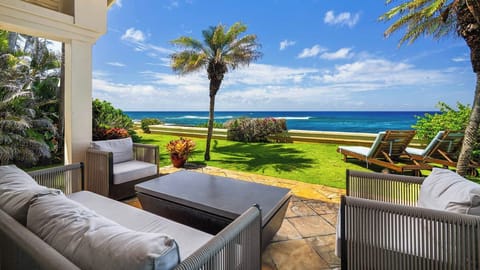 A private coastal setting where vibrant tropical landscaping frames pristine ocean vistas and manicured lawn stretches toward the shore. Palm trees stand sentinel over the beachfront grounds beneath bright island skies.
