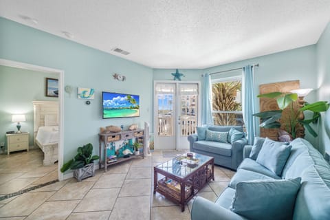 Unwind in your coastal living room with soft blue furniture, tropical touches, and balcony doors opening to ocean breezes.