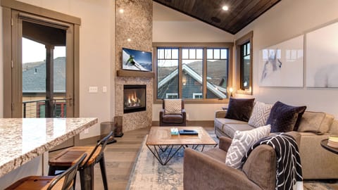Relax in this bright, open-concept living area with a stone fireplace, vaulted wood ceiling, and kitchen bar seating. The perfect spot to unwind after a day of Park City skiing!
