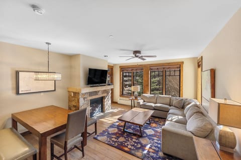 Unwind in your cozy living space featuring a stone fireplace, plush sectional, and mountain views through large windows.