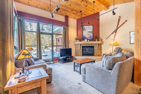 Unwind in this cozy living room with exposed wood beams, a crackling fireplace, and vintage ski decor creating alpine charm for your mountain retreat.